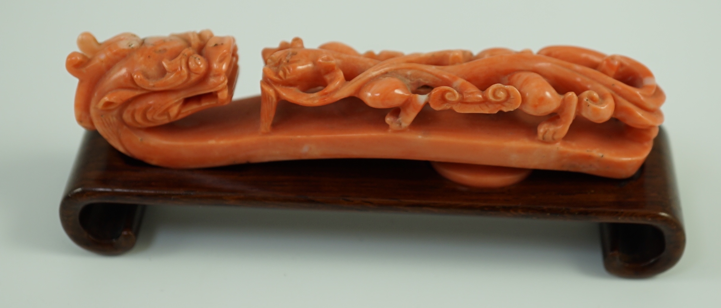 A rare Chinese coral 'dragon' belt hook 18th/19th century, 9.2 cm long, small loss to dragon horn, wood stand